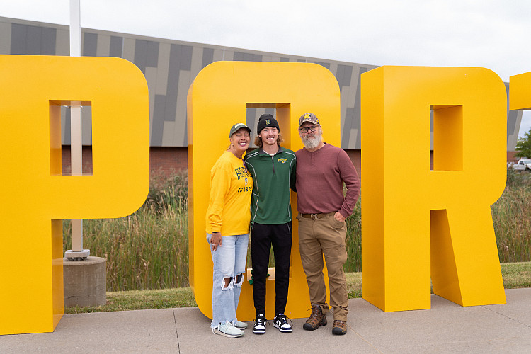 Brockport student with their parents posing in front of BPORT letters