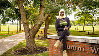 Brockport Student Government President, Tenin Sidime, sitting on the Alumni Walk's brick marker on campus.