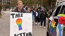 student walking in homecoming parade with a sign that says, take action.