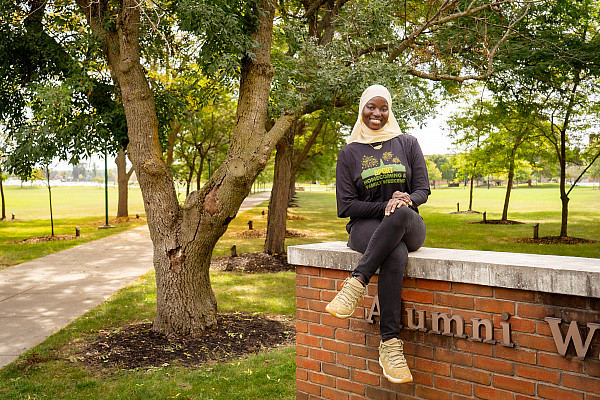 Brockport Student Government President, Tenin Sidime, sitting on the Alumni Walk's brick marker on campus.