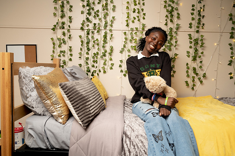 student sitting their bed in their residence hall holding a stuffed animal