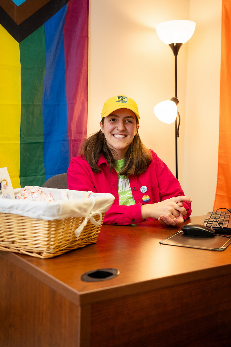 Pride flag and a student smiling sitting in the Center for Gender & Sexual Diversity on campus