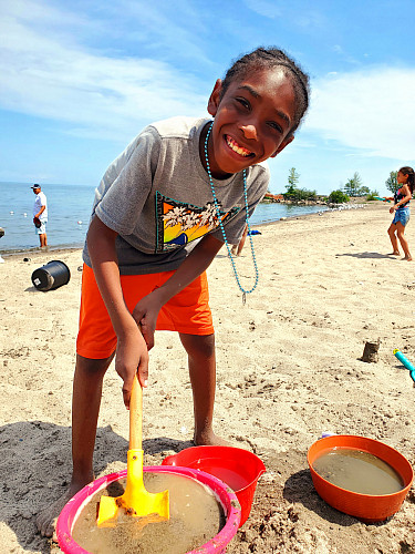 Child smiling at the camera while playing with sand at the beach