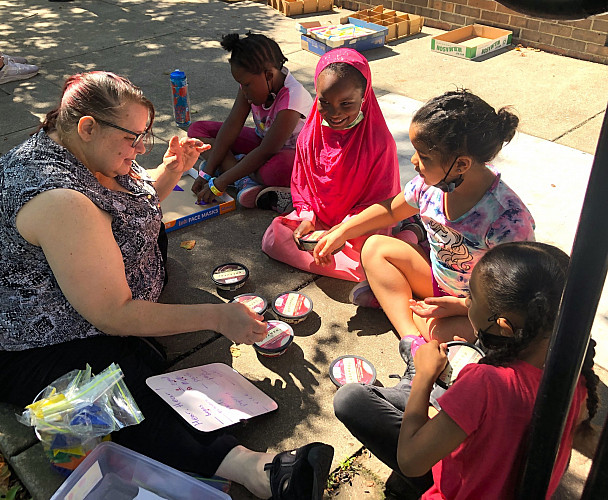 Teacher and group of children sitting outside on a sidwalk