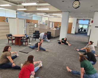 Group of SUNY Brockport staff sitting in a circle and stretching in a lobby