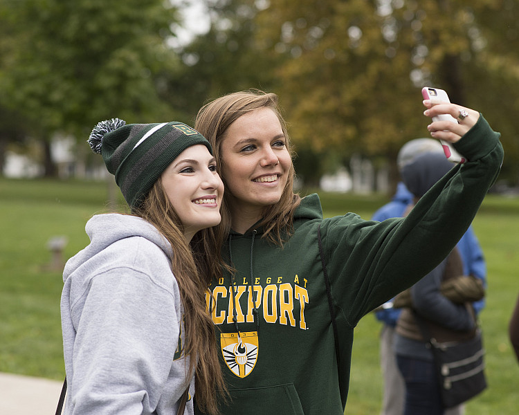 2 female Brockport Students take a selfie with a phone on SUNY Brockport's campus