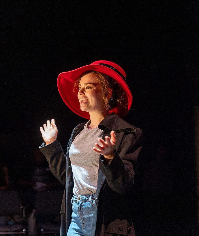 Student on stage wearing a red hat and in the middle of a performance