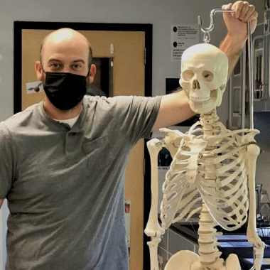 Matthew Halloran in lab standing by skeleton