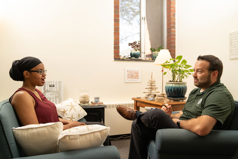 male counselor talking with female student on chairs facing each other
