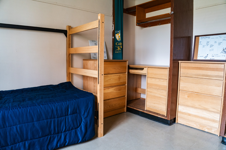 Close up of a bed, small dresser, closet space, and another dresser in a corner of a 4 person suite