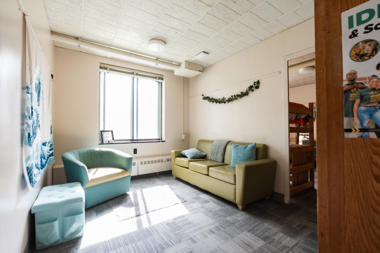 Wide view of a decorated common room of a 4 person suite with an armchair, window, and couch