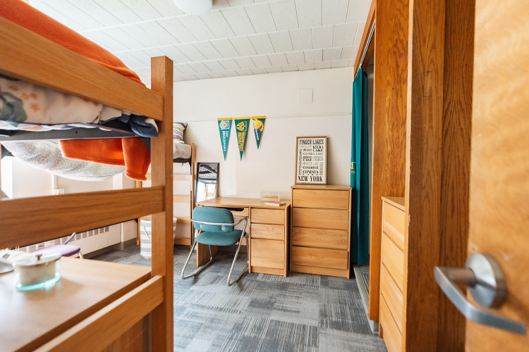 Entrance view of a bedroom with a lifted bed to the left, desk and dresser in the back, and closet space to the right