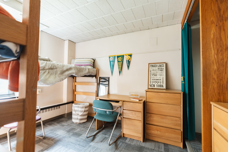 Wide view of a bedroom with 2 lifted beds to the left, a desk and dresser in the back, and closet space to the right