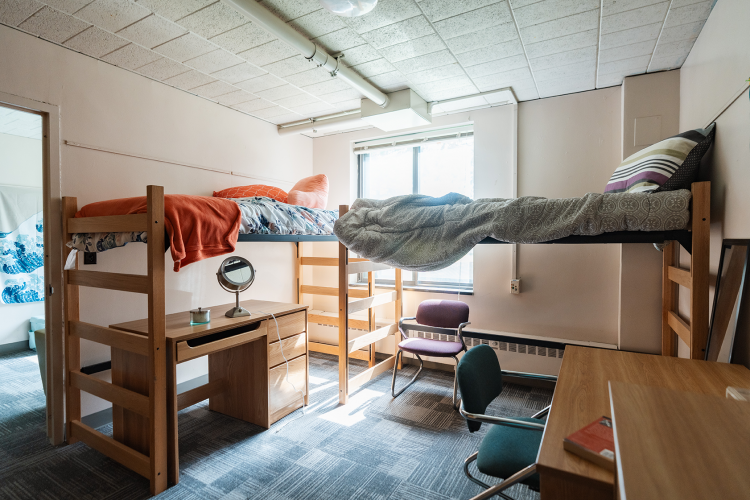 Wide view of a bedroom with 2 lifted beds with one desk underneath to the left and another desk to the right against a wall