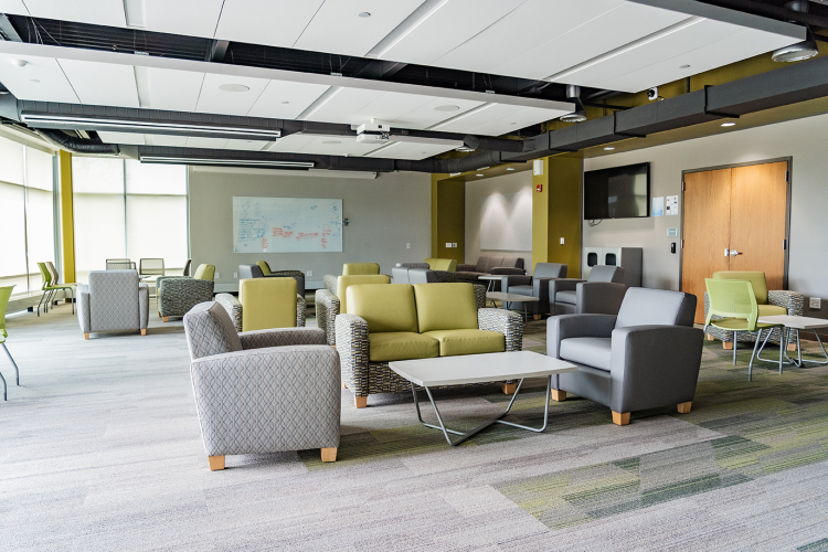 Wide view of the Eagle Hall main lobby with chairs and tables, with whiteboards and a TV mounted on the walls