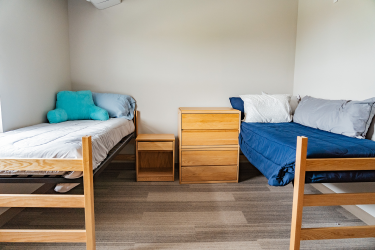 Wide view of a wall with a bed, nightstand, dresser, and another bed in a bedroom