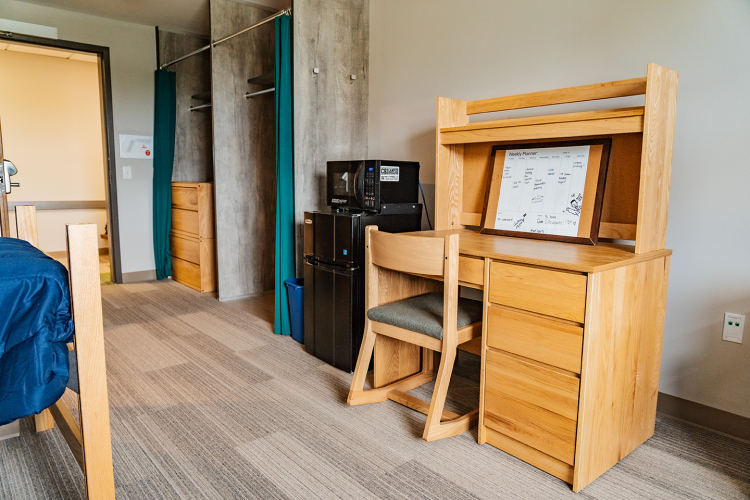 Angled view of 2 closet spaces, a fridge, microwave, and a desk with a chair in a bedroom