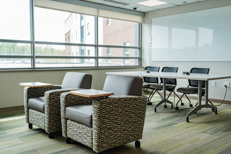 Angled view of a lounge area looking away from the TV with armchairs, a table with chairs, and a whiteboard on a wall