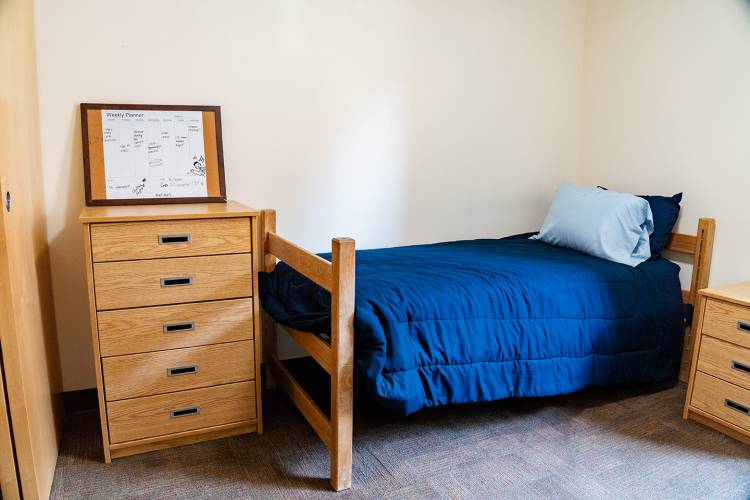 Angled view of a bedroom with a dresser, bed, and nightstand