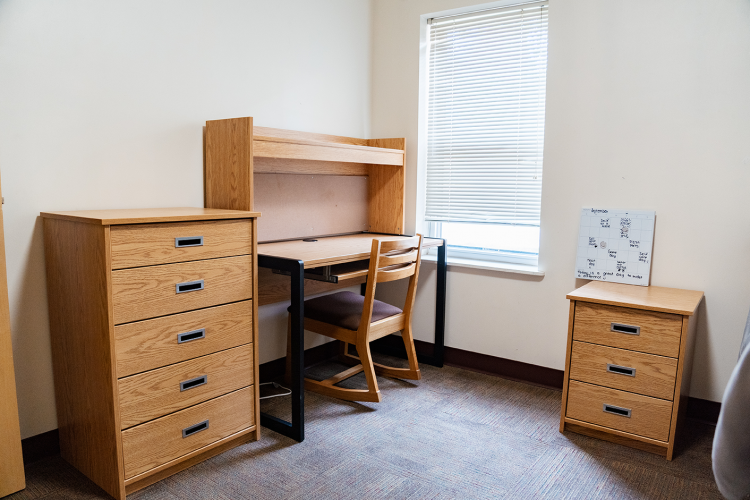 Angled view in a bedroom of a dresser, desk with a chair, and a nightstand