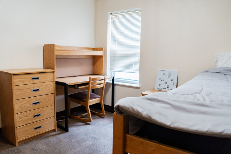 Angled view of a bedroom with a dresser, desk with chair, nightstand, and bed