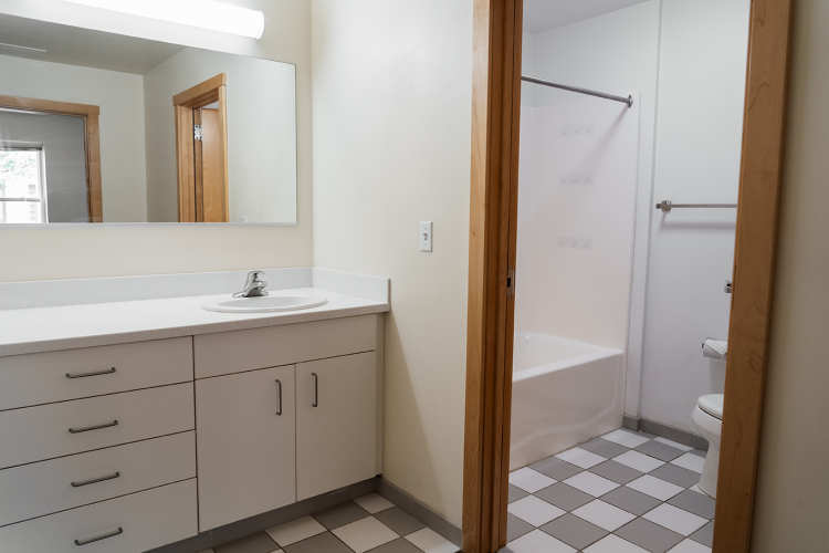 Angled view of the vanity room with a countertop, mirror and sink next to a bathroom entrance