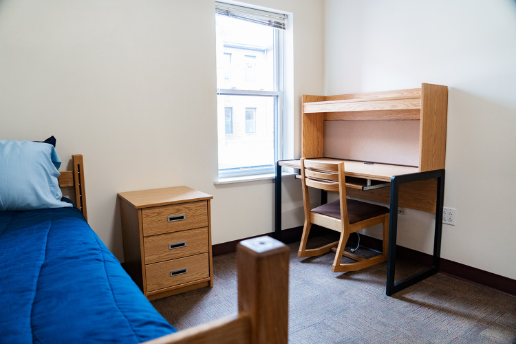 Angled view of a bedroom with a bed, nightstand, and desk with chair