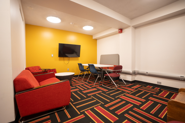 Entrance view of a lounge area with lounge chairs, chairs, table, and a wall-mounted TV