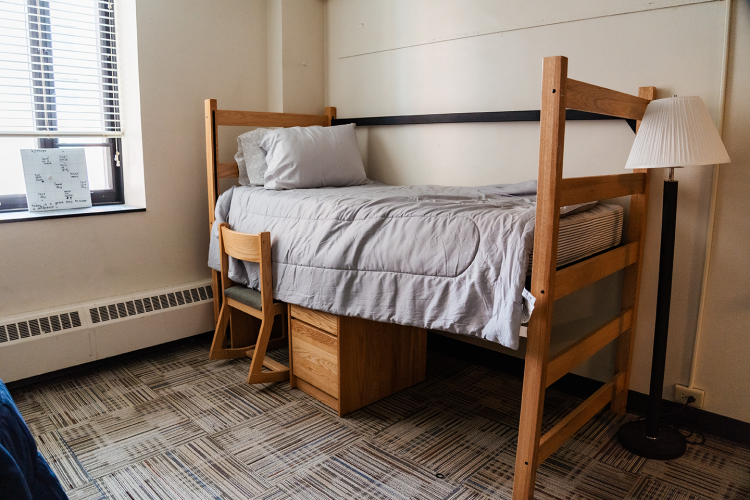 Angled view of a bedroom with a bed and a desk with chair underneath