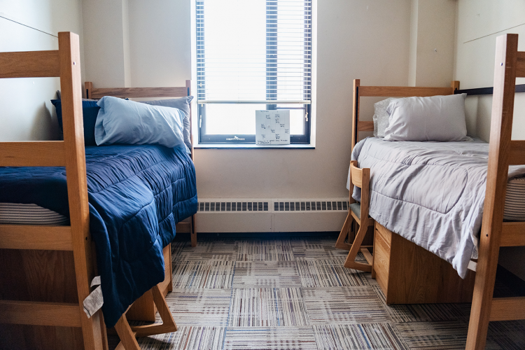 Wide view of a bedroom with a bed with a desk and chair underneath on both sides of the room