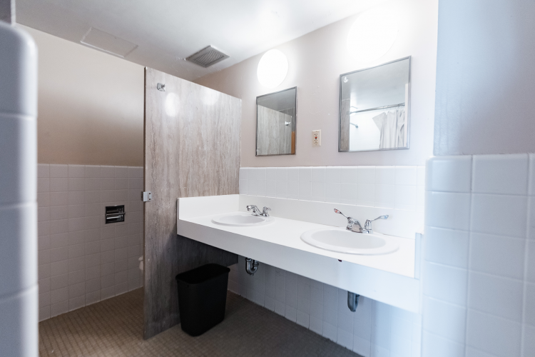Entrance view of a bathroom with a bathroom stall and 2 mirrors and sinks