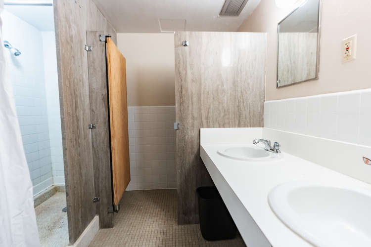 Interior view of a bathroom with a shower stall, bathroom stall, and 2 mirrors and sinks