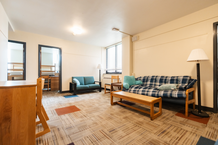 Angled view of a living room with a desk, couches, coffee table, and entrances to bedrooms