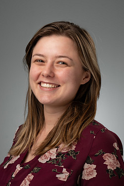 A directory photo of Paige Leary. She is smiling. She has brown hair and brown eyes. She is wearing a burgundy floral button up shirt.